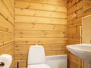 A wooden-paneled bathroom with a toilet, sink, and toilet paper.