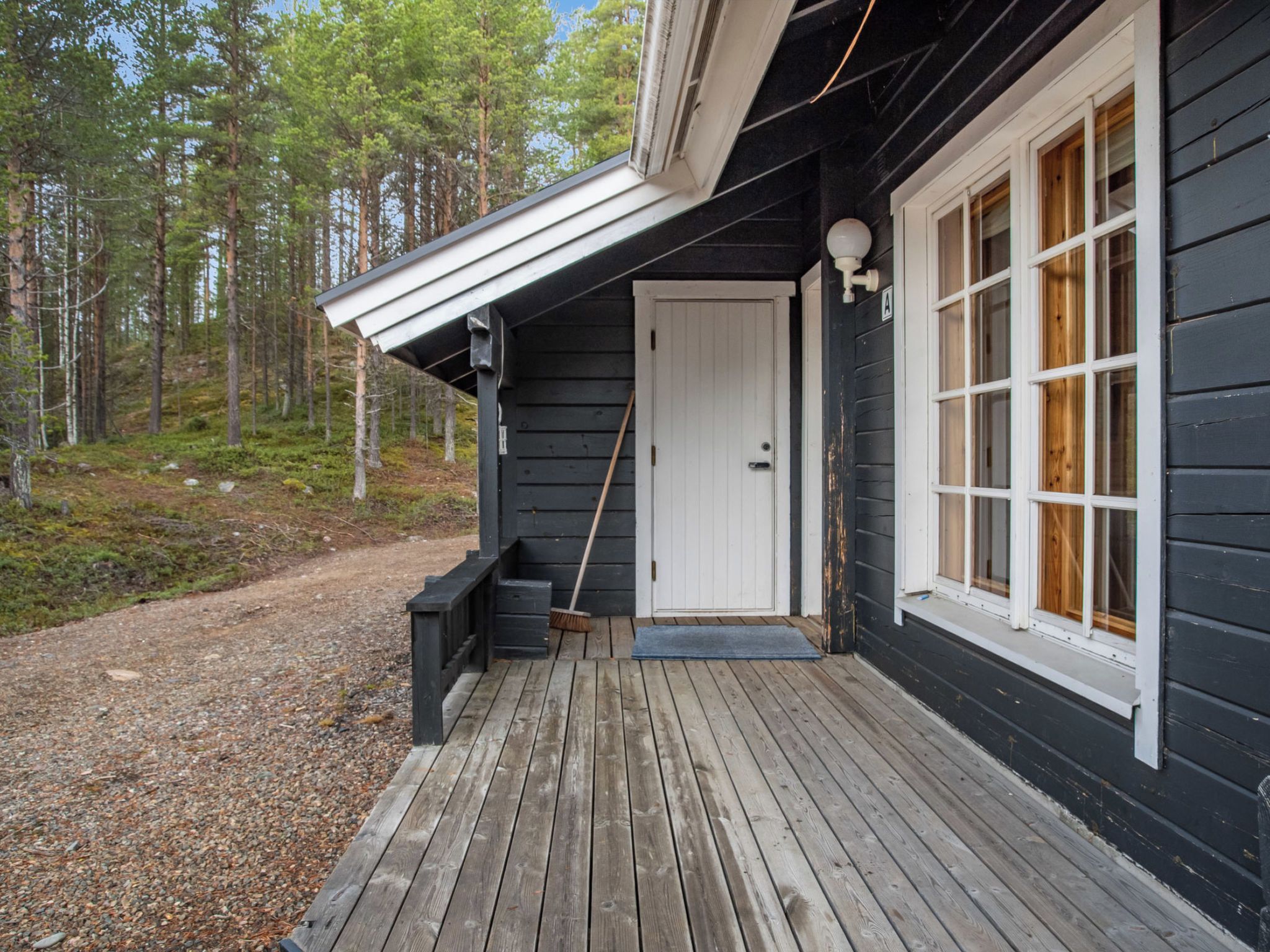 Puinen terassi johtaa tummanväriselle rakennukselle, jossa on valkoinen ovi ja ikkunat.