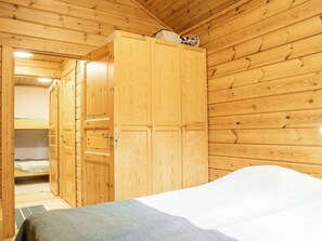 A wooden room with a bed, a wardrobe, and a door leading to another room.