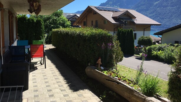 A residential area with a house featuring a sloped roof and solar panels, surrounded by lush greenery and mountains in the background. - Schwizi's Holiday Apartments by Interhome (Ringgenberg)