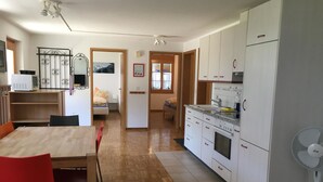 A modern kitchen with white cabinets, a built-in oven, and a microwave. There is a dining table with chairs and a fan near the kitchen. - Schwizi's Holiday Apartments by Interhome (Ringgenberg)