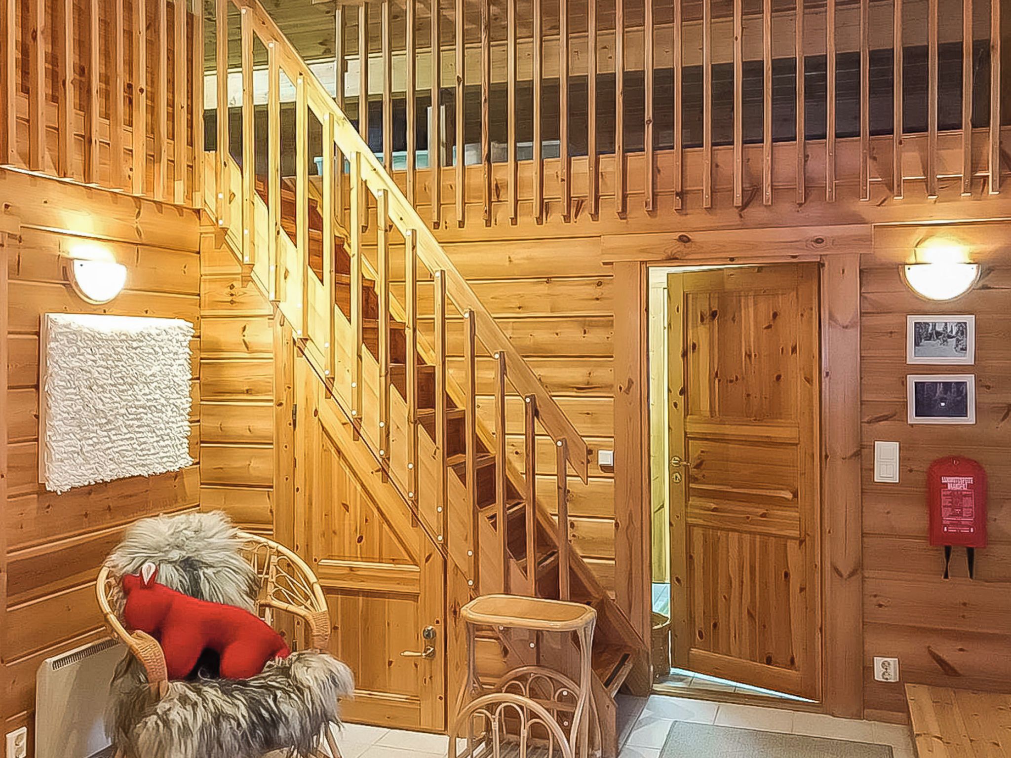 A wooden interior with a staircase, a wicker chair with a red cushion, and a small stool.