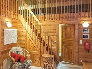 Un intérieur en bois avec un escalier, une chaise en osier dotée d’un coussin rouge et un petit tabouret.