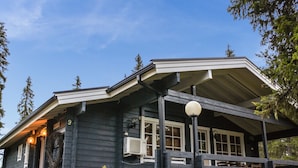 A dark wooden building with a covered porch, air conditioning units, and a small garden area. - Metsä-vuosseli rukalumous by Interhome (Kuusamo)