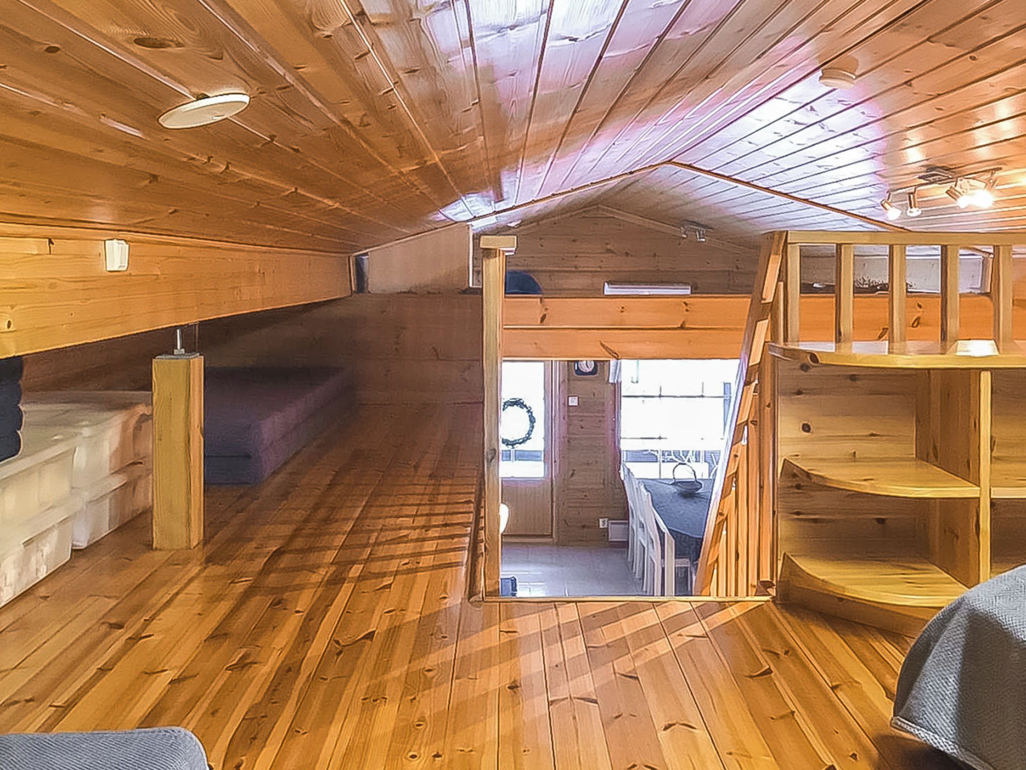 Un interior de madera con literas, una escalera y vistas a través de una puerta abierta.