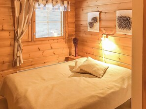 A wooden cabin room with a bed, a window with curtains, and wall-mounted artwork. - Metsä-vuosseli rukalumous by Interhome (Kuusamo)