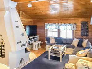 Interior acolhedor de uma cabana com sofá, televisão, lareira e mesa de jantar.