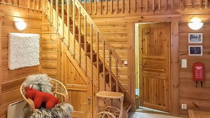 A wooden interior with a staircase, a small table, a chair, and a red object on the floor. - Metsä-vuosseli rukalumous by Interhome (Kuusamo)
