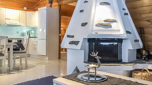 A modern kitchen with a stone-clad fireplace, wooden ceiling, and a dining area with a table and chairs. - Metsä-vuosseli rukalumous by Interhome (Kuusamo)