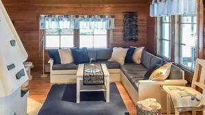 A cozy cabin interior with a sectional sofa, a small table, and a window with curtains. - Metsä-vuosseli rukalumous by Interhome (Kuusamo)