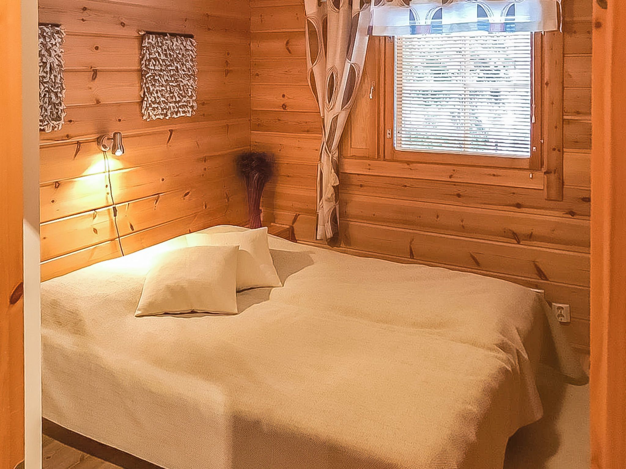 Una camera in legno con un letto, una finestra con tende e un lampadario a parete.