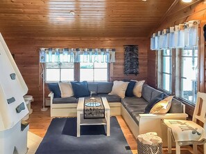 Un intérieur de chalet chaleureux avec un canapé d’angle, une petite table agrémentée d’un objet décoratif et une fenêtre avec des rideaux.