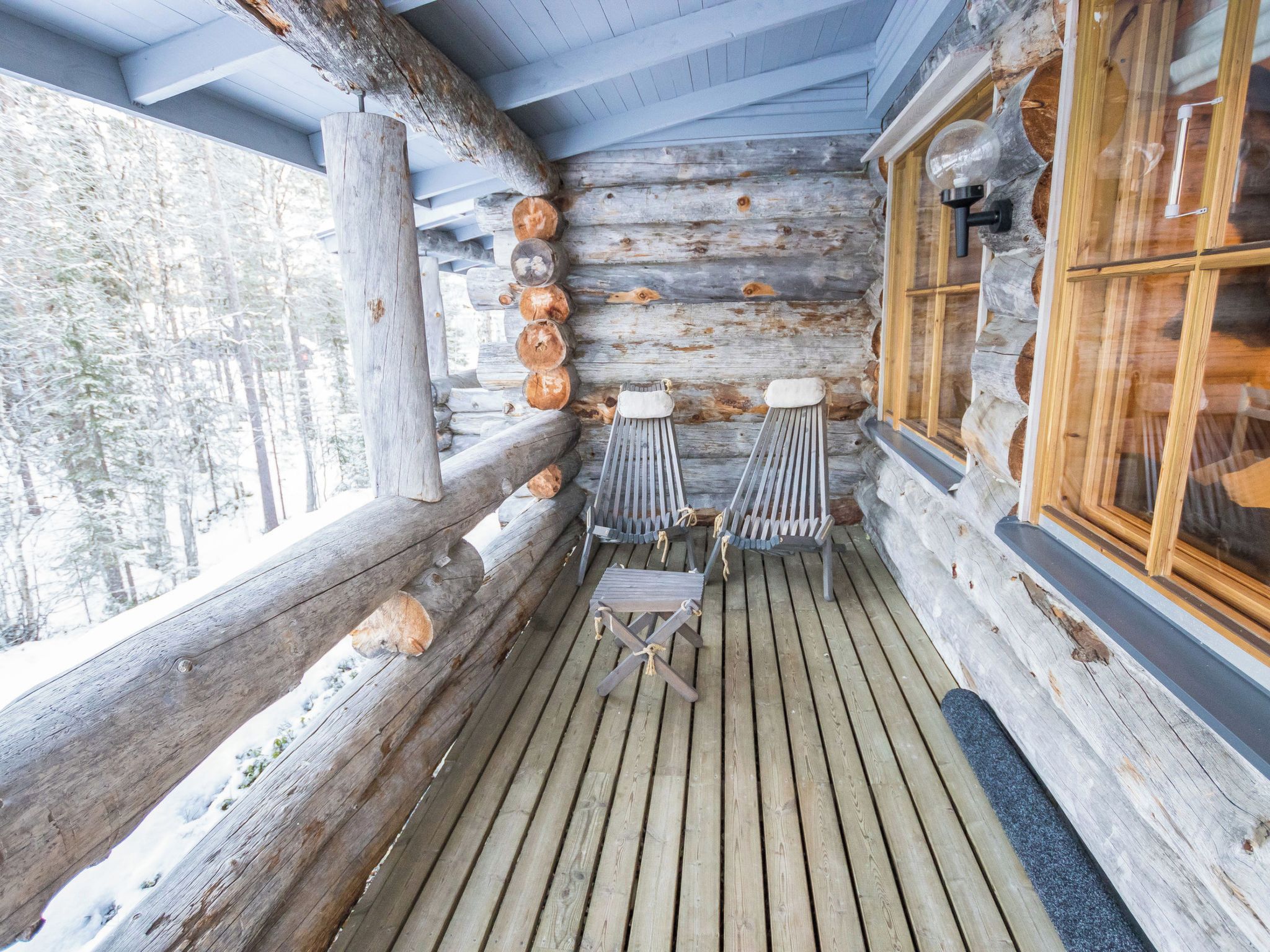 Eine Blockhütte mit einer Holzterrasse, einer Bank und einem Fenster mit Blick auf Bäume.