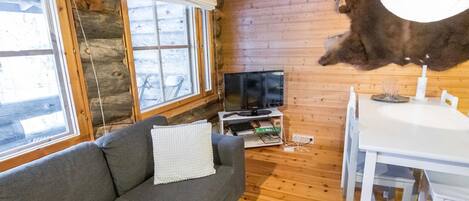 A log cabin interior with a gray sofa, a white dining table, and a mounted animal hide.