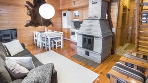 Een knus houten interieur met een stenen open haard, een eethoek en een woonkamer met een bank en een televisie.
