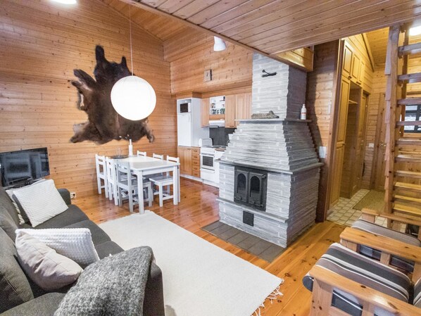 A cozy cabin interior with a stone fireplace, wooden walls, a dining area, and a living room with a sofa and a television. - Ylläsrova b5 / kasku by Interhome (Ylläsjärvi)