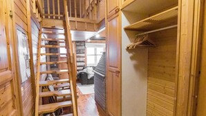 Een houten interieur met een houten trap, een kast met kledingroede, en een stenen muur op de achtergrond.