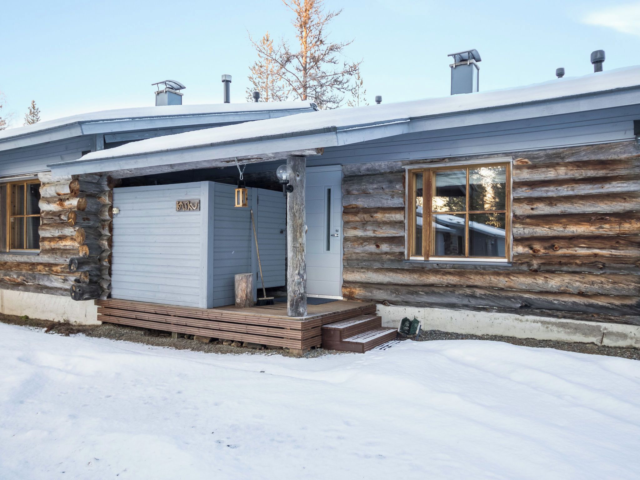 En hytte med garage, trætrapper og et snedækket tag.