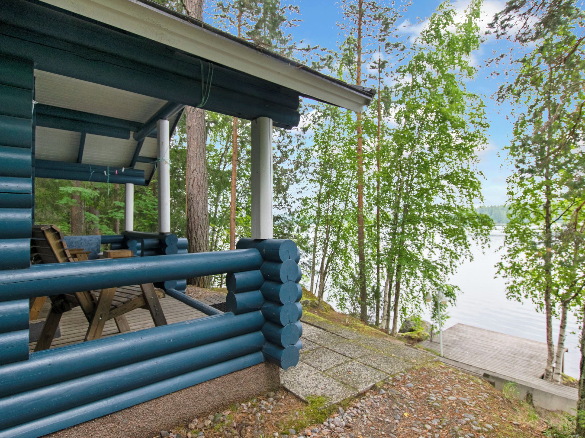 Una baita di legno con una veranda che si affaccia su un lago, circondata da alberi.