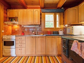 Une cuisine avec des meubles de rangement en bois, une cuisinière, un four à micro-ondes et une fenêtre.