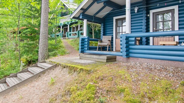 Une cabane en rondins dotée d’une véranda, de bancs en bois et d’un escalier menant à l’entrée.