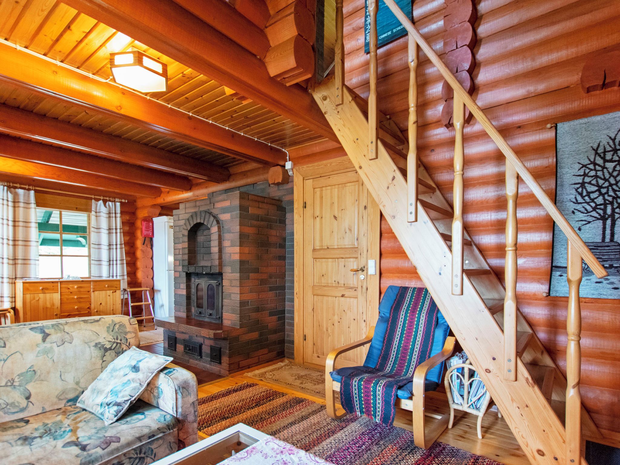 Ein Blockhaus-Interieur mit Kamin, einer Holztreppe und einer gemütlichen Sitzecke.