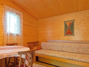 Een gezellig cabin interieur met houten plafond, een eettafel met stoelen, een bank en een raam met bloemen gordijnen.