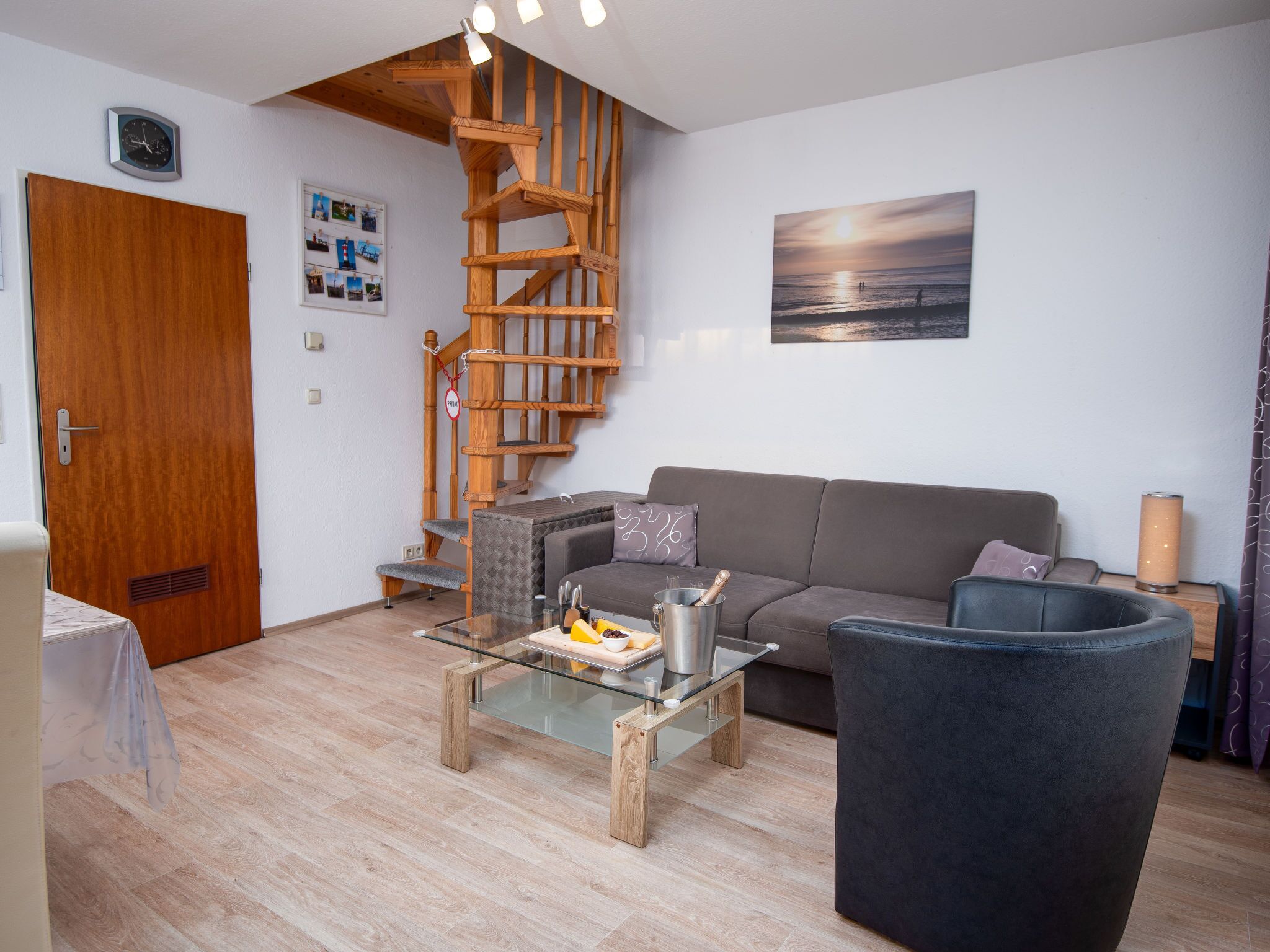 Uma sala de estar moderna com escada de madeira, sofá cinza, mesa de centro de vidro e poltrona preta.