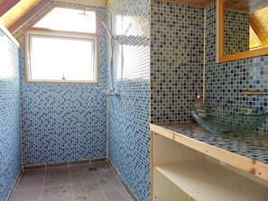 Ein Badezimmer mit blauen Mosaikfliesen, einem Fenster und einem Waschbecken aus Glas auf der Ablagefläche.