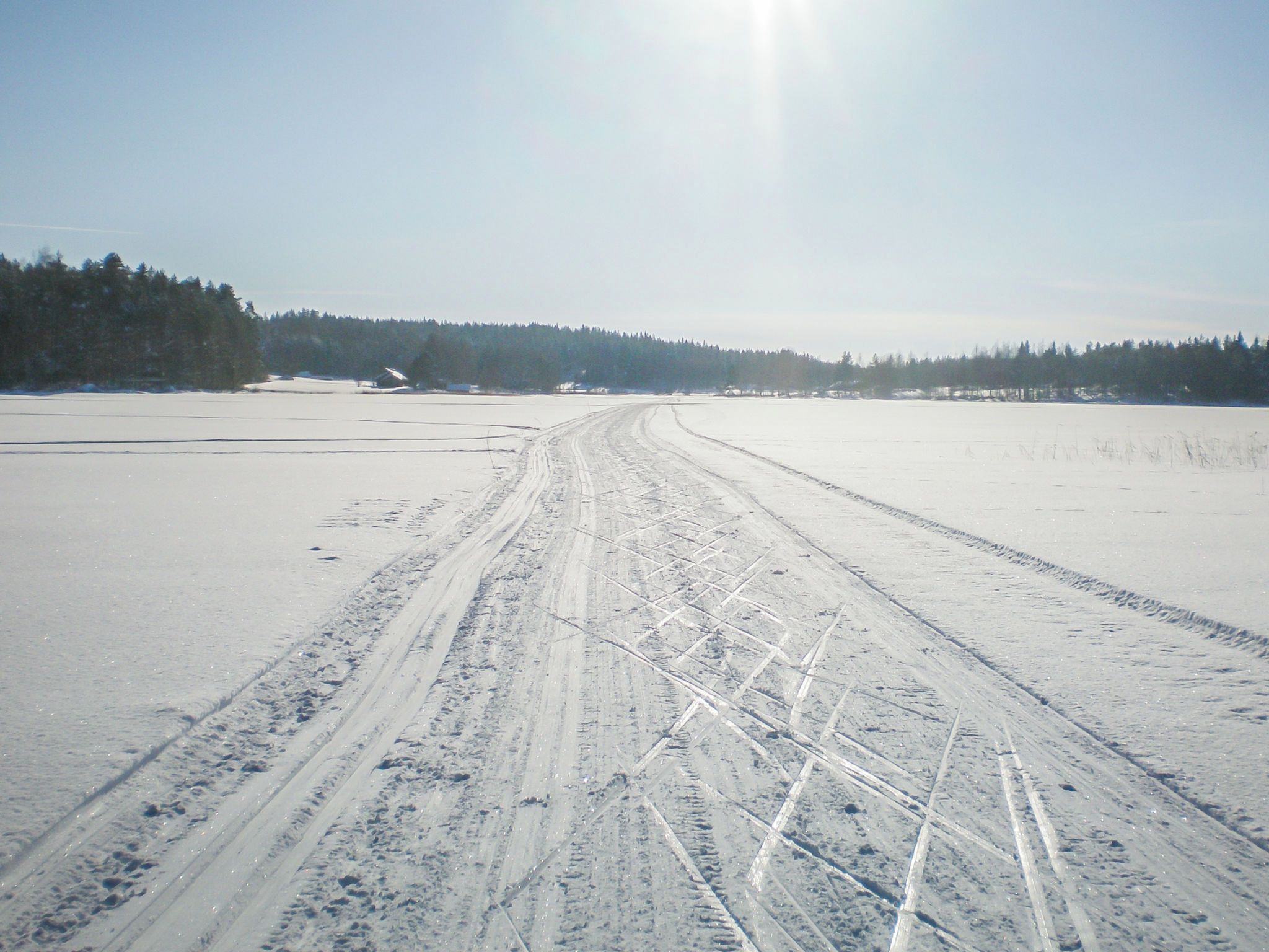 A snowy landscape with a clear sky and a road with tire tracks.