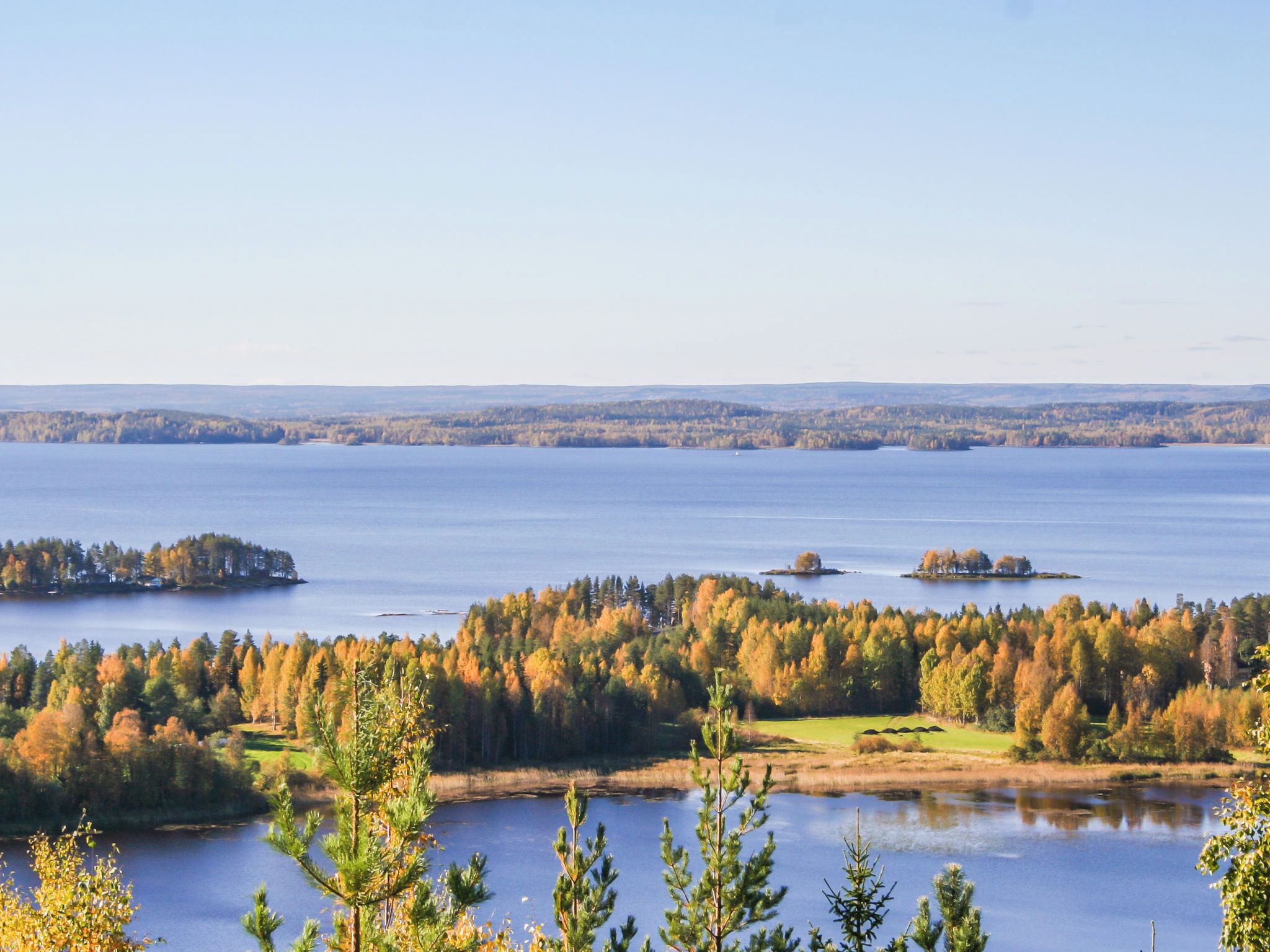 A panoramic view of a lake surrounded by forested land with clear skies.