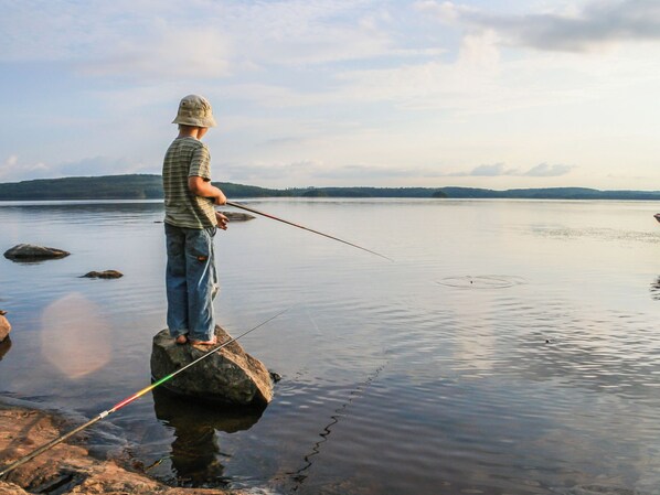 A person standing on a rock by a calm body of water, holding a fishing rod.