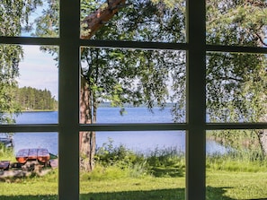Une vue à travers une fenêtre donnant sur un paysage naturel, comprenant une étendue d’eau et des arbres.