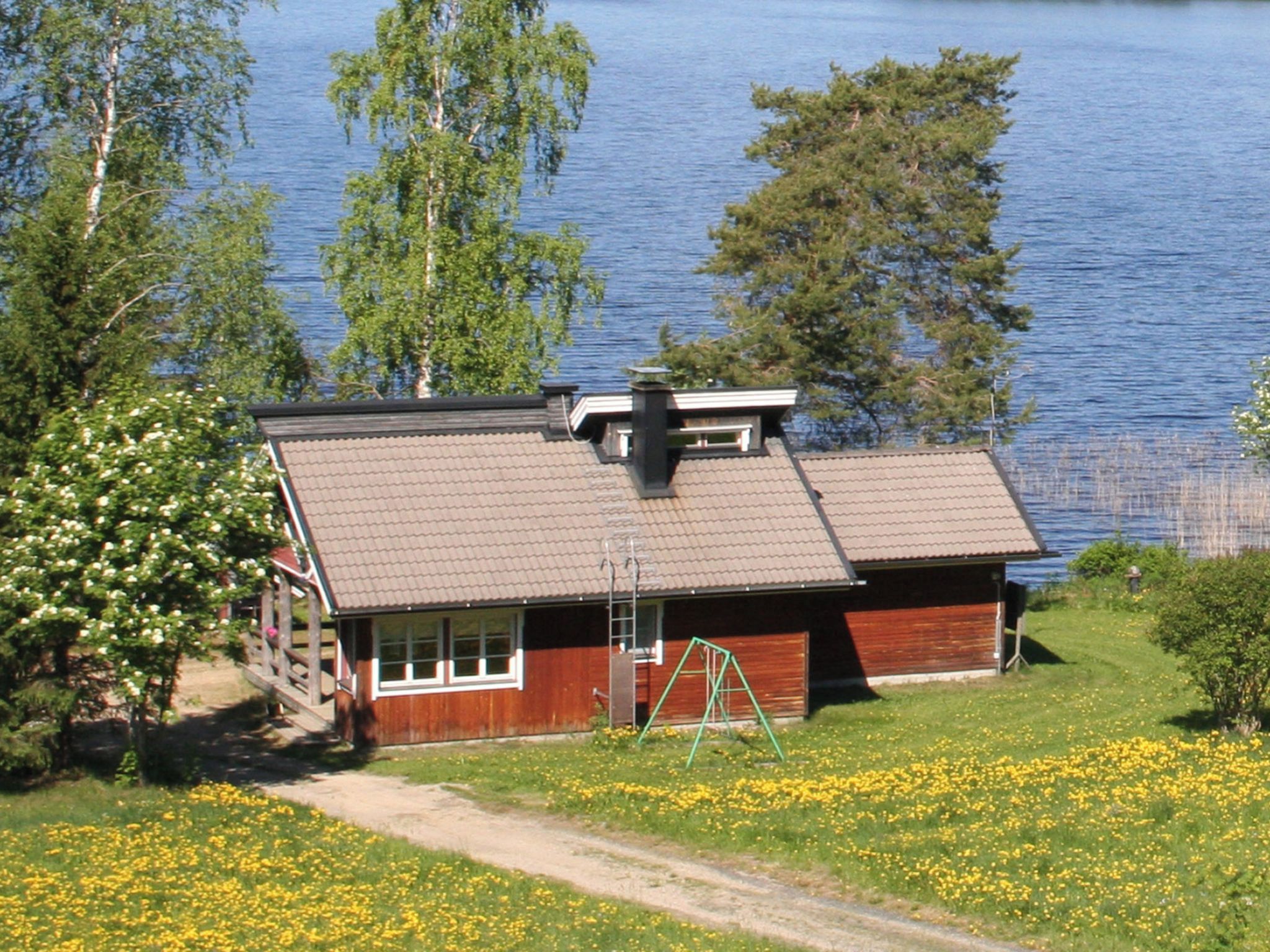 En stuga av trä med ett sluttande tak, en skorsten och en gunga framför.