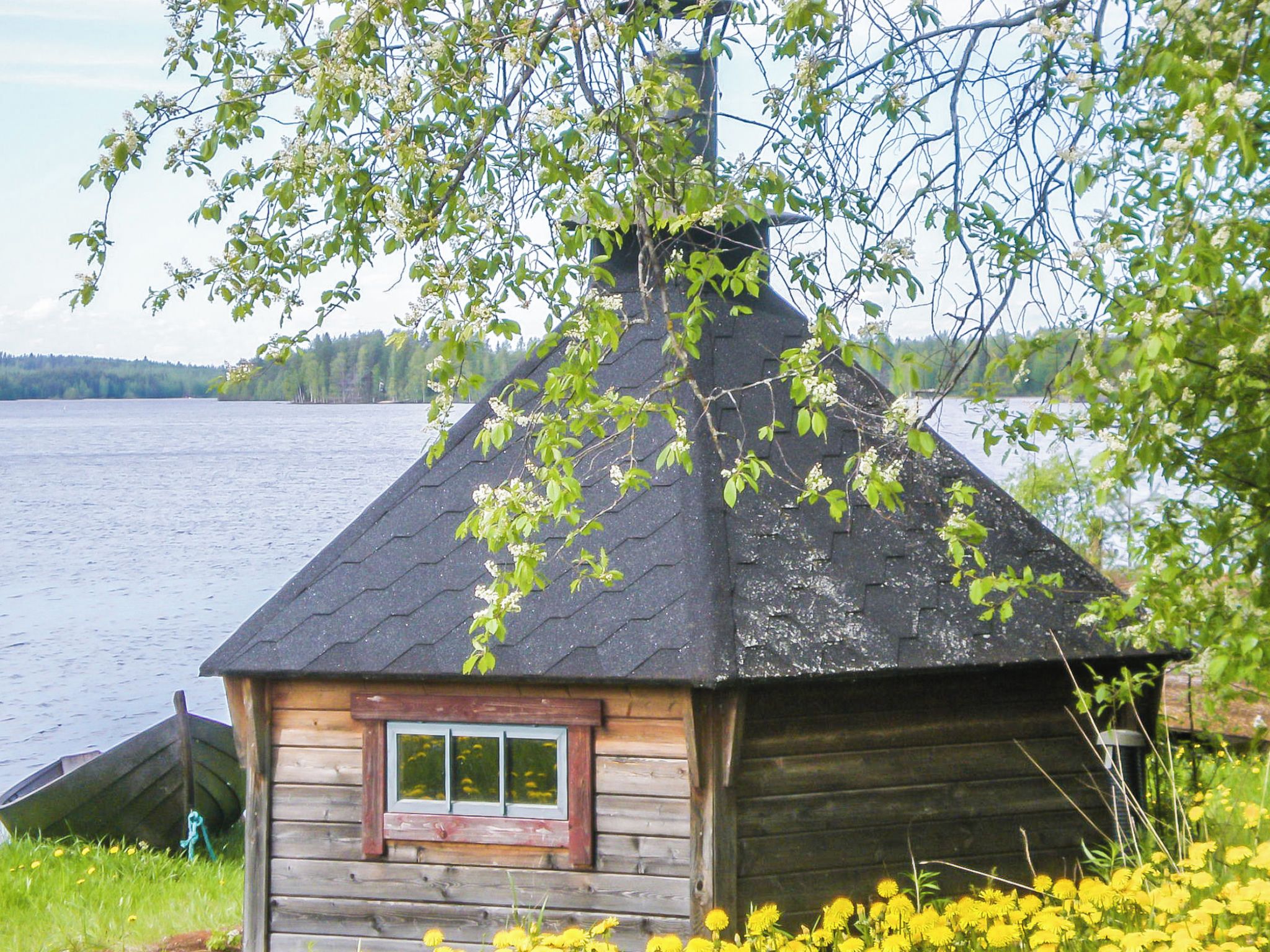 Eine hölzerne Hütte mit einem Fenster, umgeben von Grünpflanzen und einem Gewässer.