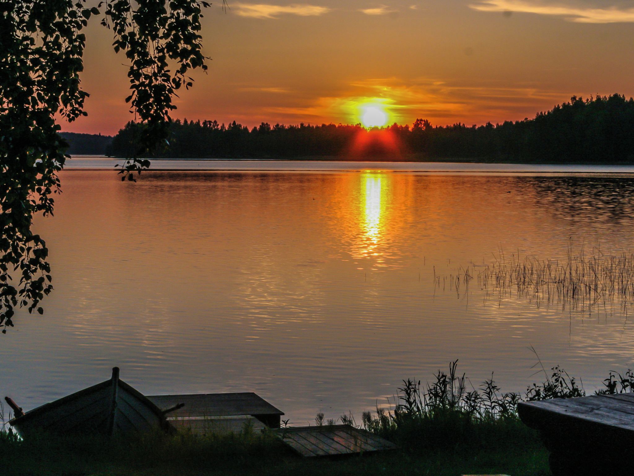 A sunset over a calm lake with a dock and a small building in the foreground.