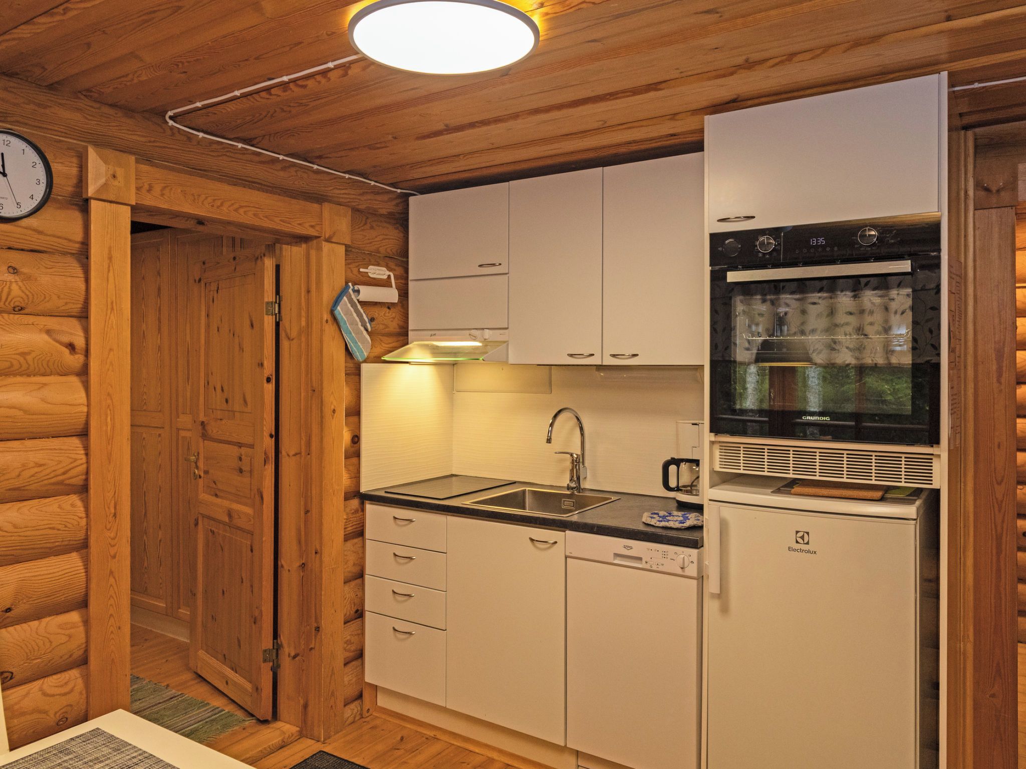 A compact kitchen with wooden walls, a sink, a stove, and a refrigerator.