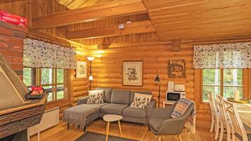 L’intérieur d’un chalet confortable, avec une cheminée, un ensemble de canapés, une table à manger et des chaises, ainsi que des œuvres d’art encadrées accrochées aux murs.