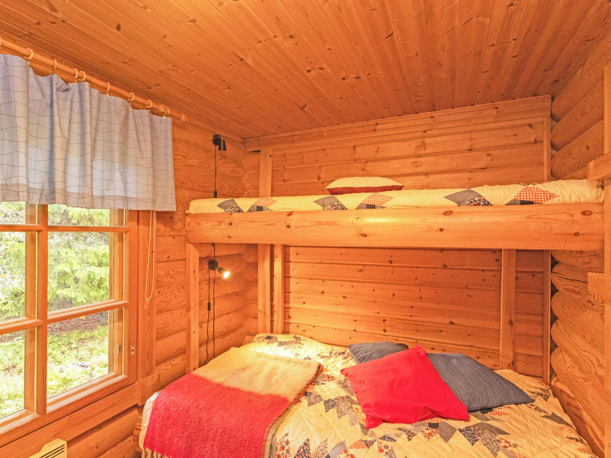Una stanza in una baita di legno con un letto a castello, una finestra con tende e un letto con molti cuscini.