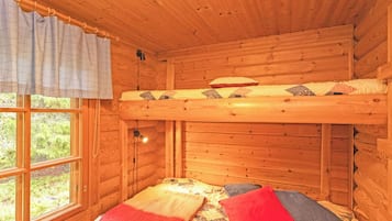Una stanza in una baita di legno con un letto a castello, una finestra con tende e un letto con molti cuscini.