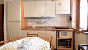A compact kitchen with white cabinets, a wooden countertop, a sink, a microwave, and a stove. - Gondar Studio by Interhome (Aci Trezza)