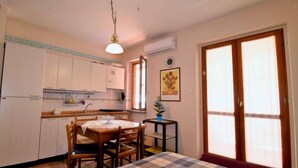 A compact kitchen with white cabinets, a dining table with chairs, a hanging light fixture, and a window with a view. - Gondar Studio by Interhome (Aci Trezza)