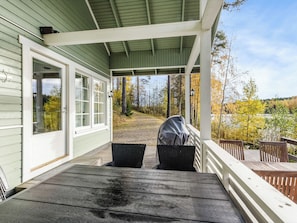 A covered porch with a view of a forest and a lake.