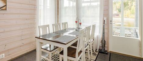 A dining area with a wooden table and chairs, a patterned rug, and a view of a lake through a window.