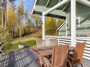A wooden deck with a table and chairs, surrounded by trees with autumn foliage.