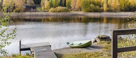 A wooden dock extending into a calm lake with a green boat on the shore.