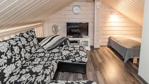 A cozy attic bedroom with a wooden sloped ceiling, a TV, a bed, and a sofa with patterned cushions.