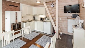 A compact kitchen with white cabinets, a wooden staircase, a flat-screen TV, and a white refrigerator.