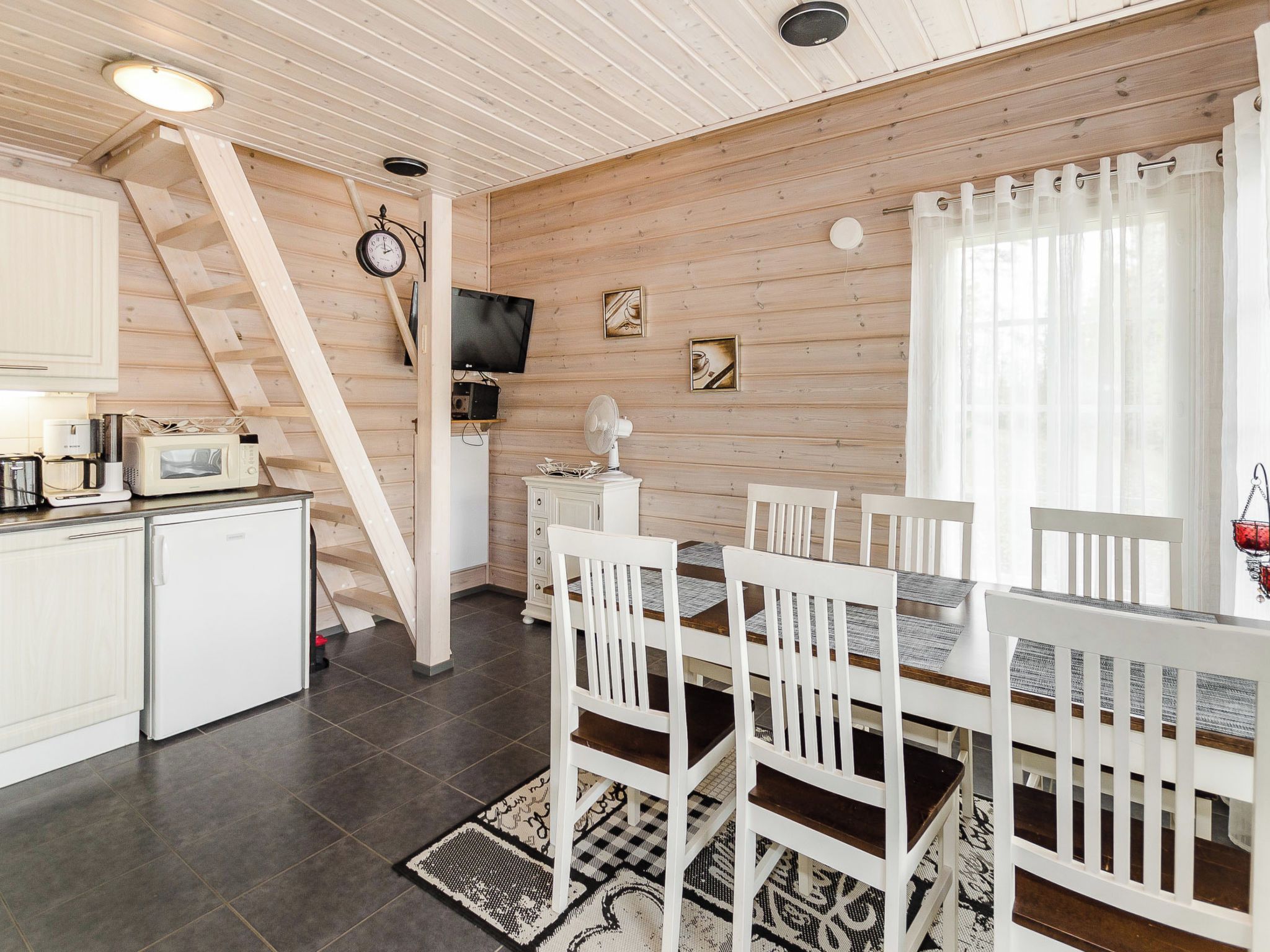 A kitchen with white cabinets, a microwave, a stove, and a sink. There is a dining table with white chairs and a black and white patterned rug.