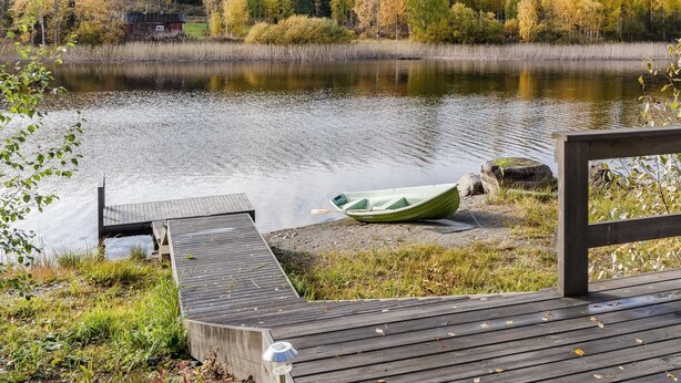 A wooden dock extending into a calm lake surrounded by autumn-colored trees.